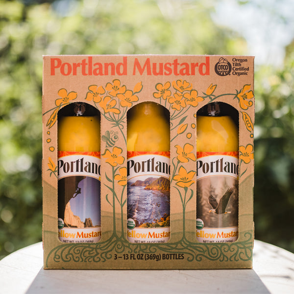 Portland Organic Mustard 3-Bottle Gift Pack sitting on a table outside, no GMOs, Gluten Free, Dairy Free