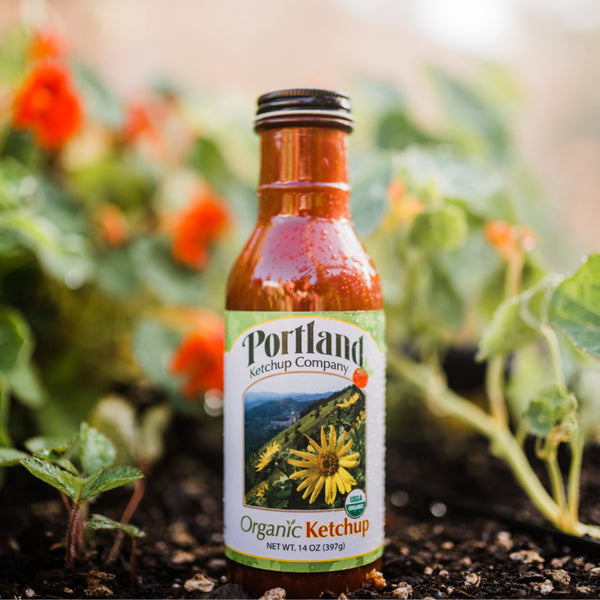 Bottle of Portland Organic Ketchup sitting in a garden, gluten free, dairy free, non GMO condiment